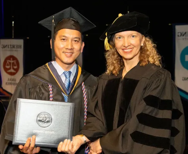 Herzing University graduation ceremony, professor shaking hands with a graduate holding their diploma.